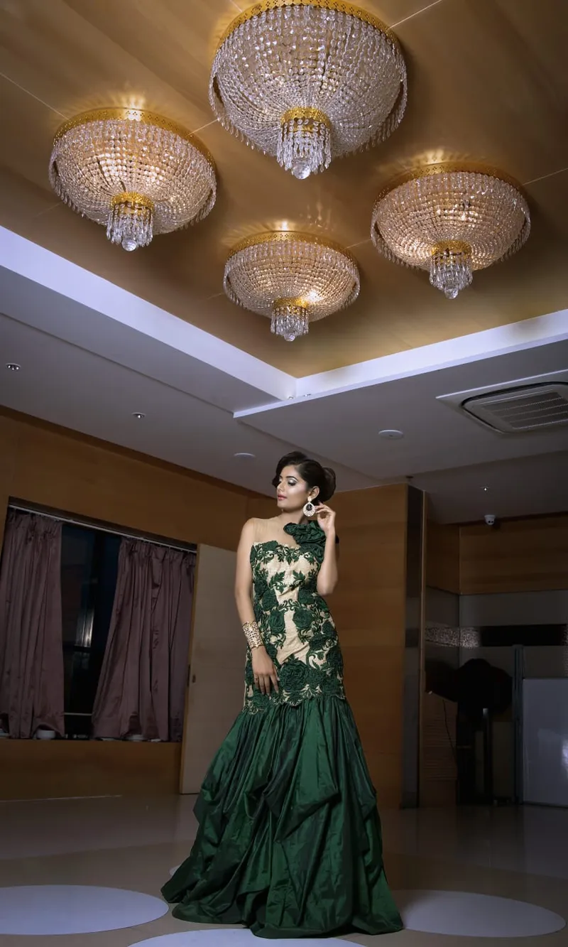 Snehal Patil in a green gown beneath crystal chandeliers