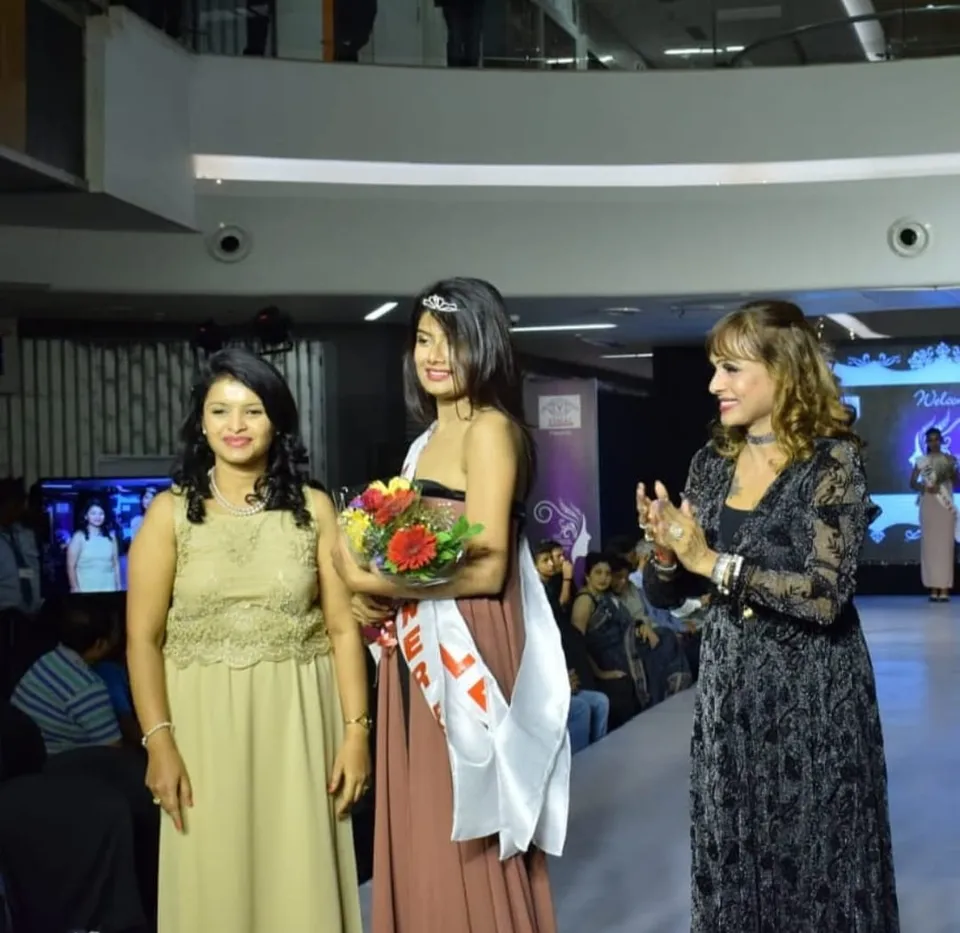 Snehal Patil on a runway stage with a sash and a bouquet
